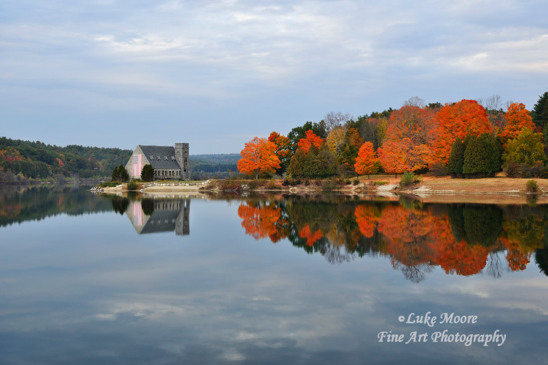 A peaceful and scenic autumn afternoon at the Wachusett Reservoir in West Boylston, Massachusetts, MA, Worcester County. The iconic Old Stone Church is surrounded with vivid orange fall foliage. The clouds form unique patterns in the sky and upon the reservoir water. "Afternoon Reflections" by Luke Moore.