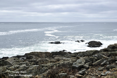 Mostly cloudy, seascape photograph of the Marginal Way in Ogunquit, Maine, ME during a spring morning. The sun peeks through just a little bit to illuminate the sky and the white, frothy water. The Margin is a walkway that spans a scenic portion of Maine's coast and the Atlantic Ocean. The Marginal way was started in 1925 with a donation of land made by Josiah Chase. The walkway has been preserved and managed by Ogunquit’s Marginal Way Committee with help from a non-profit called the Marginal Way Preservation Fund. 